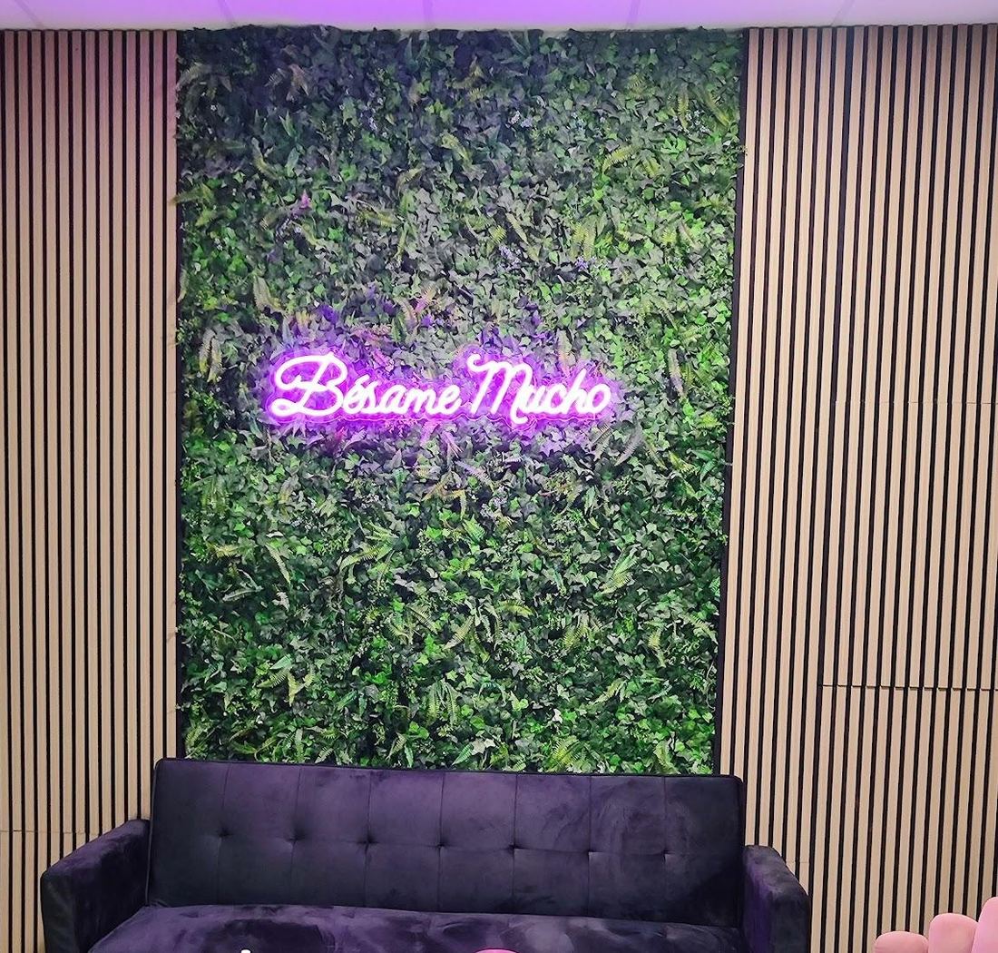 La pared verde con el neón «Bésame Mucho» y el sofá de terciopelo
